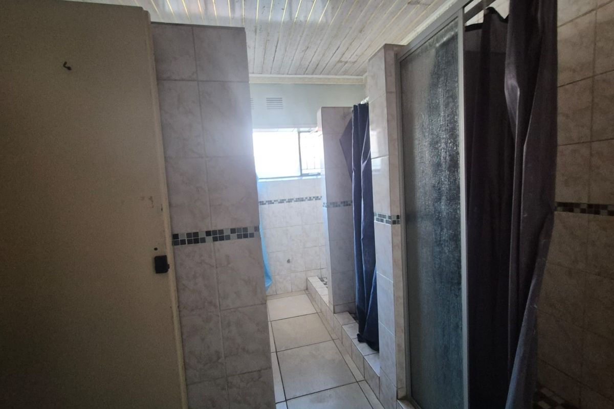 A functional bathroom featuring multiple shower stalls with tiled finishes and a timber ceiling, requiring cosmetic updates to modernize the space.