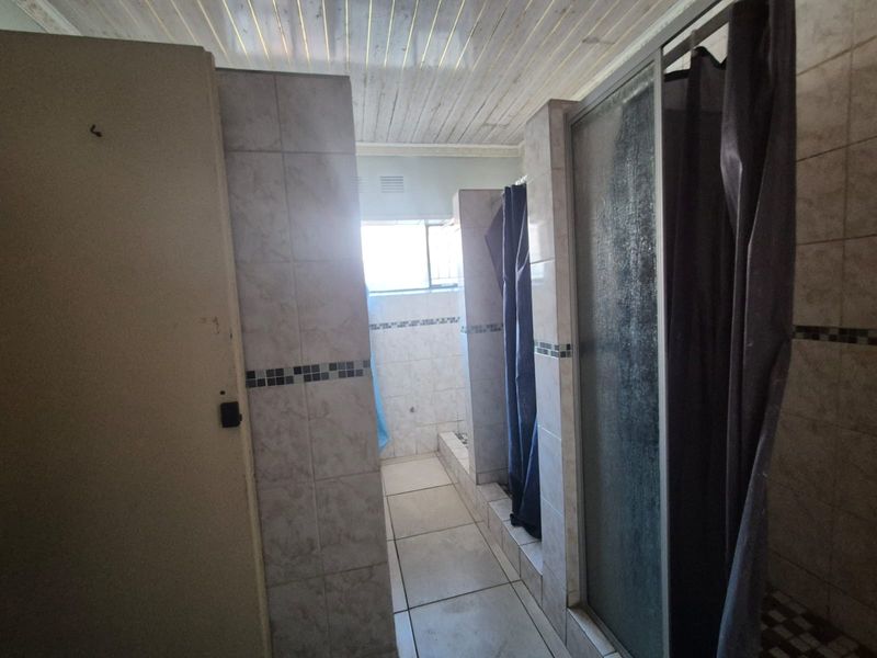 A functional bathroom featuring multiple shower stalls with tiled finishes and a timber ceiling, requiring cosmetic updates to modernize the space.