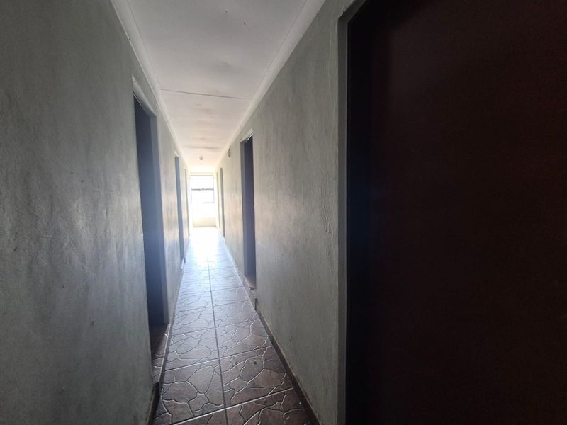 A narrow residential hallway featuring tiled flooring and multiple doorways leading to various rooms, requiring cosmetic updates to improve the overall finish.