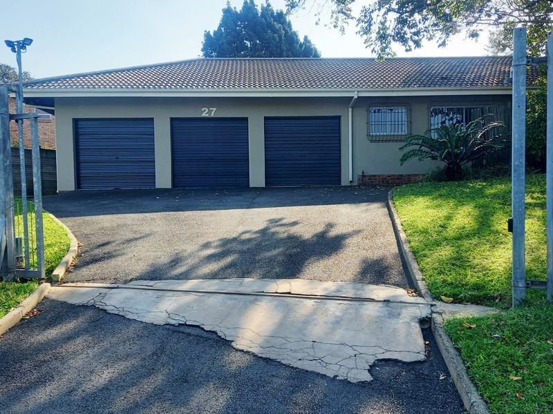 Front view of a residential property featuring a triple garage, tiled roof, and a paved driveway with a security gate.