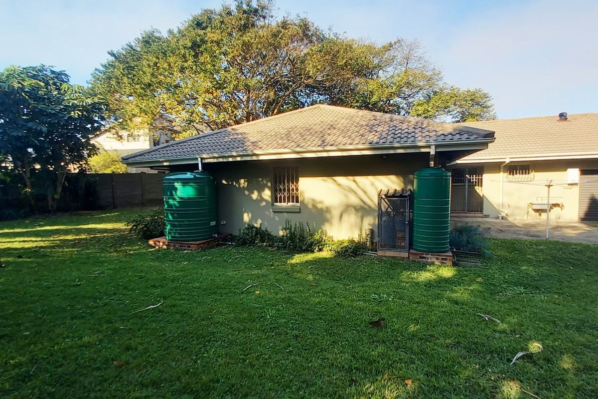 Rear view of the property featuring a well-maintained lawn, tiled roof structure, and two installed water storage tanks.