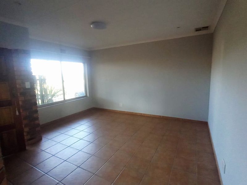 An empty living room featuring tiled flooring, a brick fireplace, and natural light from a large window.