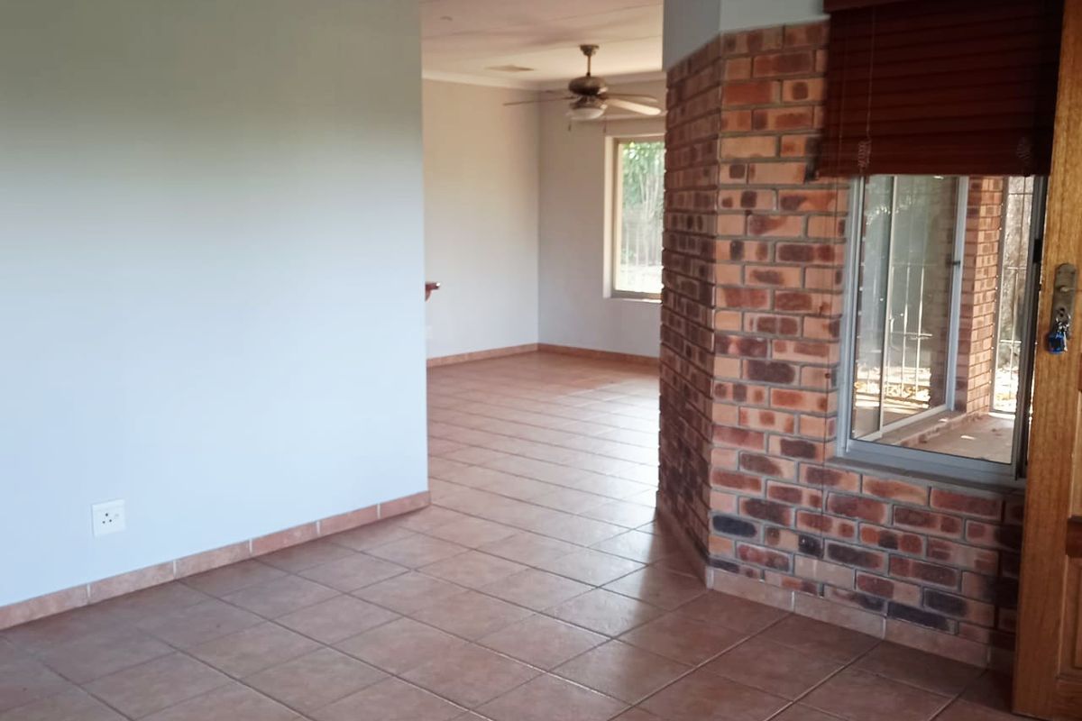An open-plan living area featuring ceramic floor tiles, an exposed brick feature wall, and a ceiling fan, offering a versatile blank canvas.