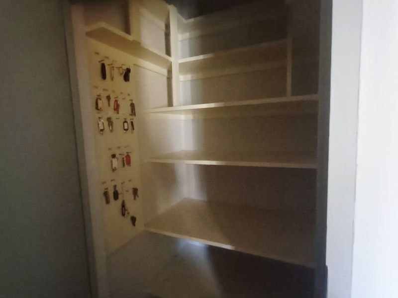 A small utility storage closet featuring built-in shelving and a wall-mounted key organization rack.