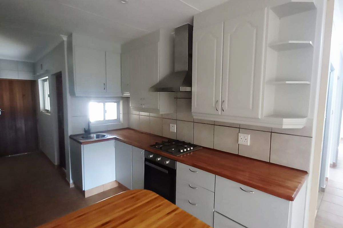A clean, functional kitchen featuring white cabinetry, warm wooden countertops, a built-in oven, gas hob, and a stainless steel extractor fan.