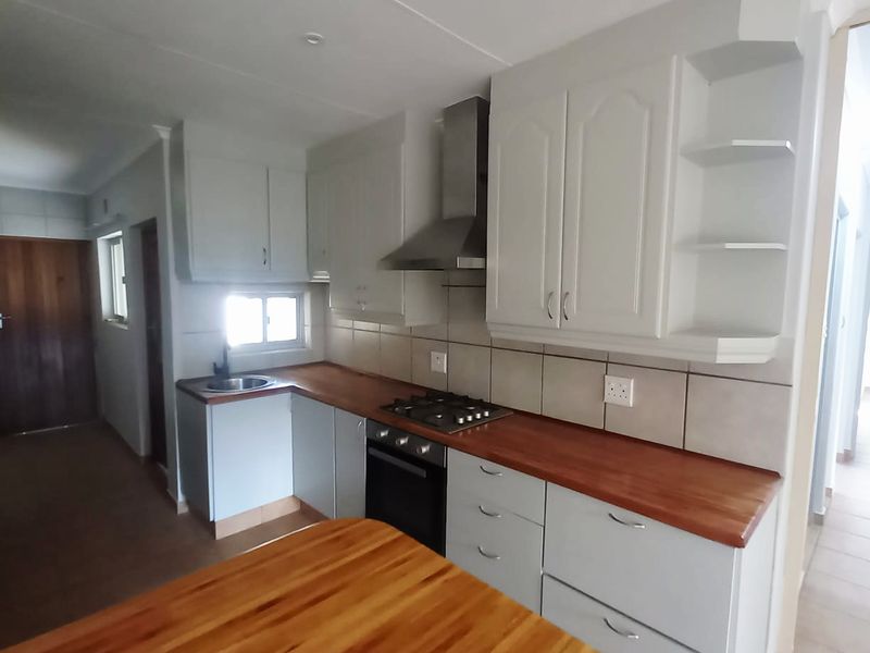 A clean, functional kitchen featuring white cabinetry, warm wooden countertops, a built-in oven, gas hob, and a stainless steel extractor fan.