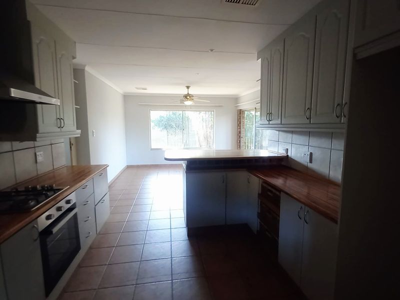 An open-plan kitchen and living area featuring wooden countertops, built-in cabinetry, a gas hob, and tiled flooring throughout.