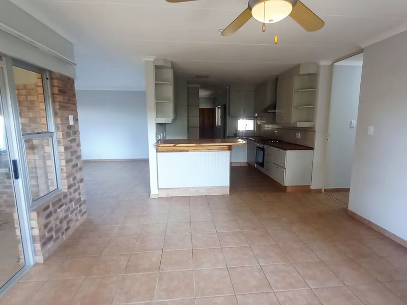 Spacious open-plan living and kitchen area featuring tiled floors, a breakfast bar, built-in cabinetry, and a ceiling fan, with access to an outdoor area.