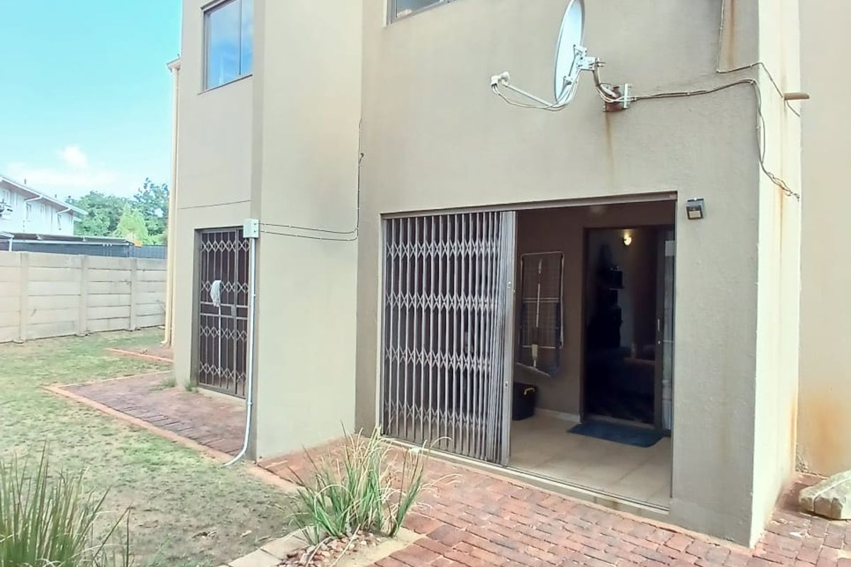 Rear view of the townhouse featuring a brick paved patio, sliding glass doors with security gates, and a private garden area.