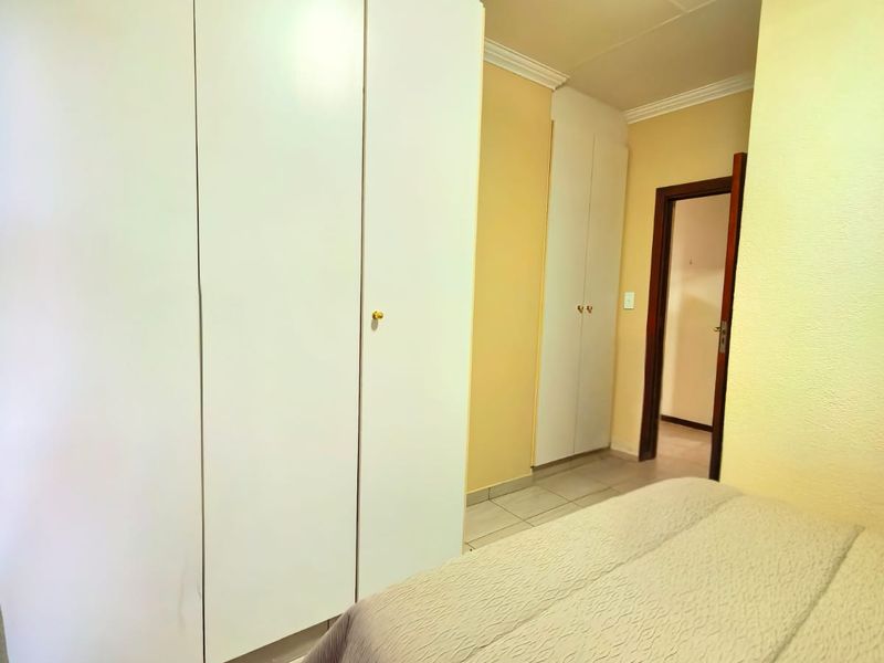 A bedroom featuring built-in cupboards, tiled flooring, and decorative cornicing, providing a functional and neutral living space.