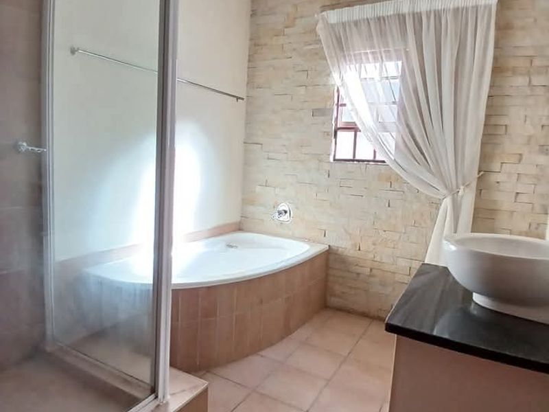 A well-appointed bathroom featuring a built-in bathtub, a separate glass shower enclosure, a stone-clad feature wall, and a modern vessel sink vanity.