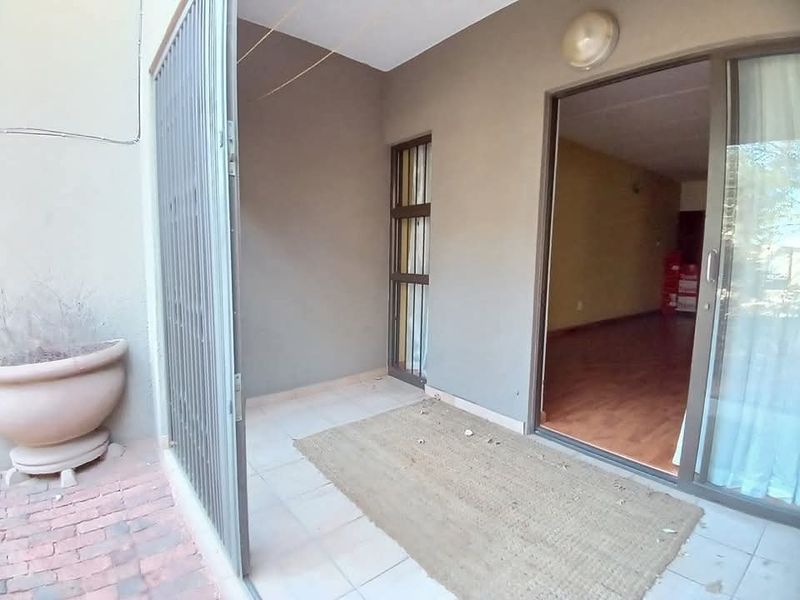 A covered patio area featuring tiled flooring, a security gate, and direct access to the interior living space through a sliding glass door.