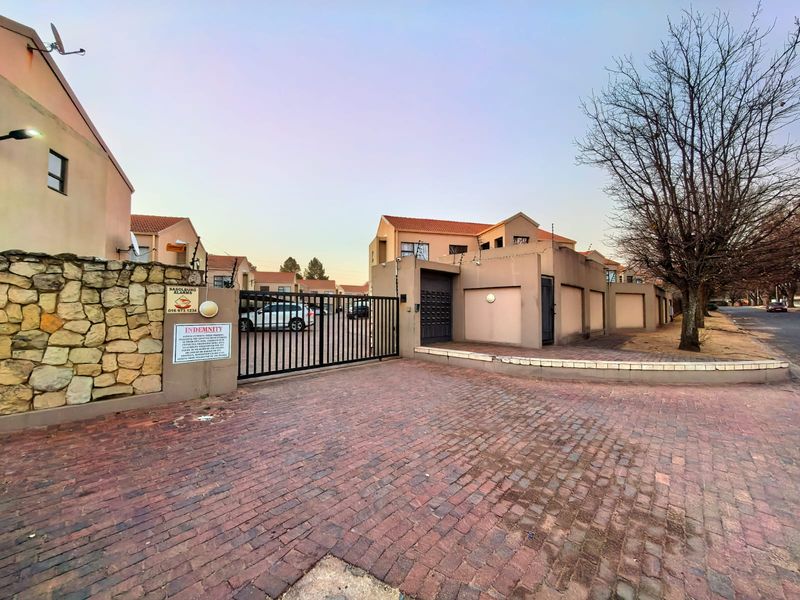 Front entrance of the townhouse complex featuring a secure gated access point, paved driveway, and perimeter walling with stone accents.