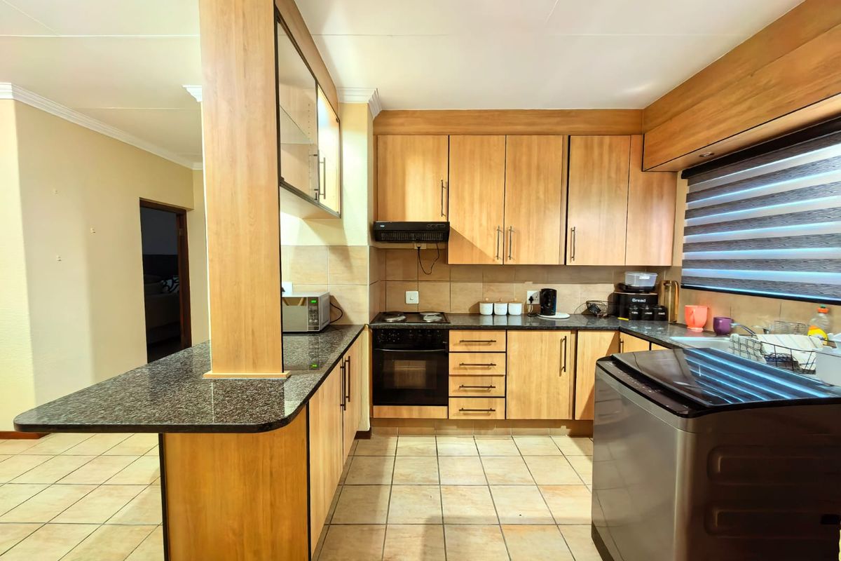 Functional kitchen featuring laminate cabinetry, granite countertops, built-in oven, electric hob, extractor fan, and a breakfast bar with tiled flooring.