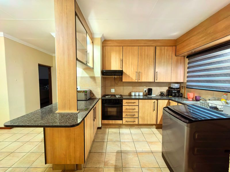 Functional kitchen featuring laminate cabinetry, granite countertops, built-in oven, electric hob, extractor fan, and a breakfast bar with tiled flooring.