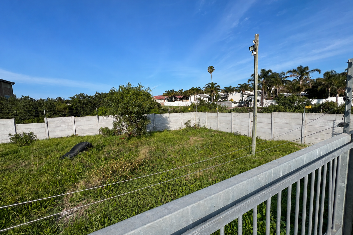 A vacant residential plot featuring a perimeter precast concrete wall, electric fencing, and a security floodlight, ready for development.