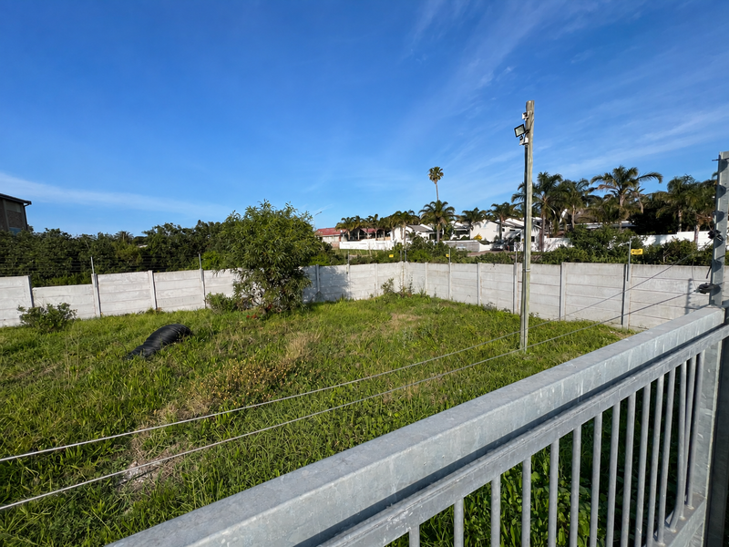 A vacant residential plot featuring a perimeter precast concrete wall, electric fencing, and a security floodlight, ready for development.