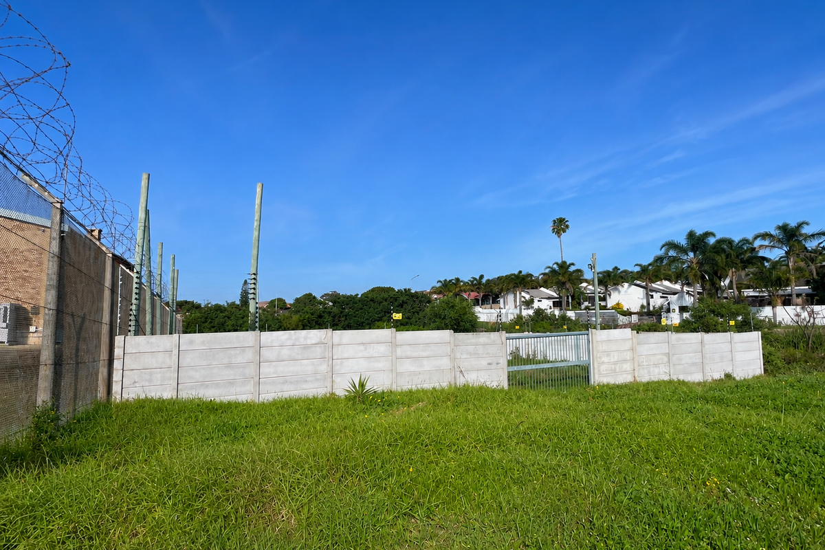 A vacant residential plot featuring a precast concrete boundary wall, electric fencing, and razor wire security measures.