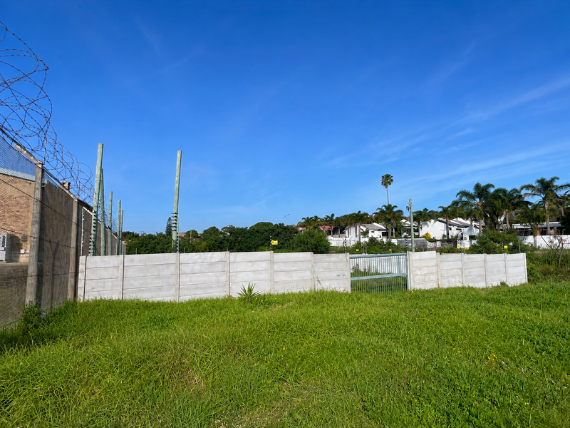 A vacant residential plot featuring a precast concrete boundary wall, electric fencing, and razor wire security measures.