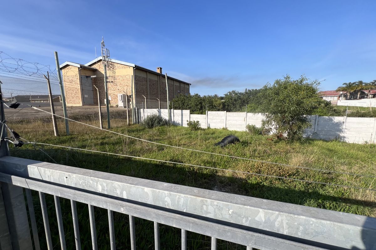 A vacant residential plot featuring a grassed area, enclosed by a precast concrete wall and electric fencing.