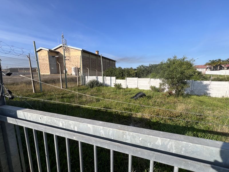 A vacant residential plot featuring a grassed area, enclosed by a precast concrete wall and electric fencing.