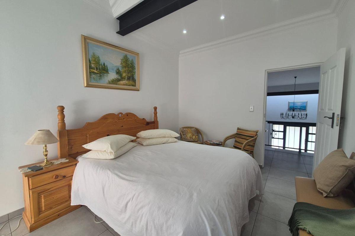 A spacious bedroom featuring tiled flooring, recessed downlighting, and an exposed structural steel beam, with an open doorway leading to an adjacent landing area.