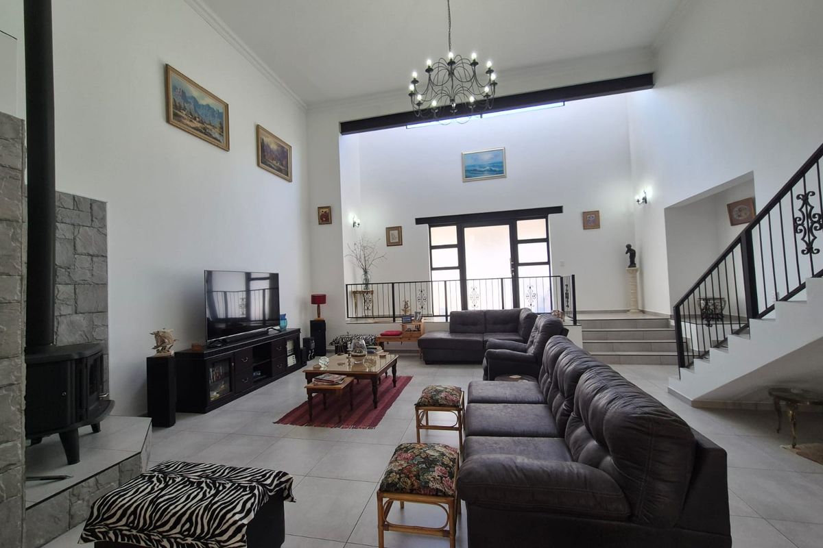 Spacious open-plan living area featuring high ceilings, a stone-clad fireplace, tiled flooring, and a staircase with decorative metal railings.