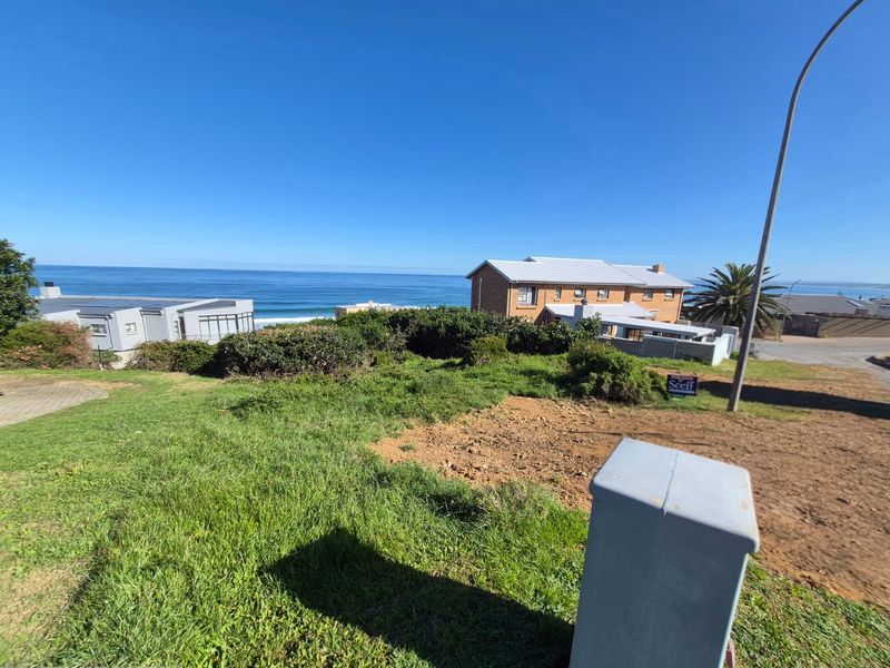 A vacant residential plot featuring a gentle slope, established lawn, and an electrical utility box, offering scenic ocean views in a coastal neighborhood.