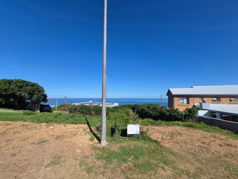 A vacant residential plot offering an expansive ocean view, featuring a utility pole and natural coastal vegetation.