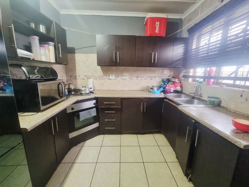 A functional kitchen featuring dark built-in cabinetry, granite countertops, a built-in oven, and a stainless steel sink with tiled backsplash and flooring.