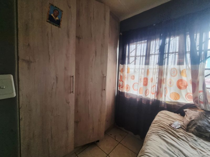 A bedroom featuring built-in wooden cupboards, tiled flooring, and a window with security bars.
