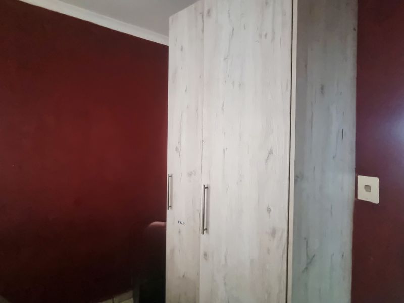 A bedroom featuring a light-toned wood-effect built-in wardrobe against deep red walls.
