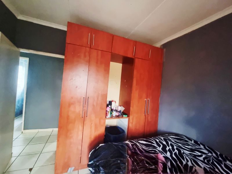 A bedroom featuring built-in wooden cupboards and tiled flooring, requiring cosmetic updates to improve the overall aesthetic and condition.