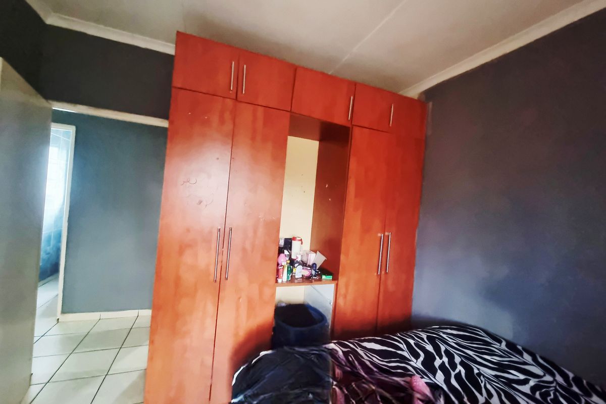 A bedroom featuring built-in wooden cupboards and tiled flooring, requiring cosmetic updates to improve the overall aesthetic and condition.