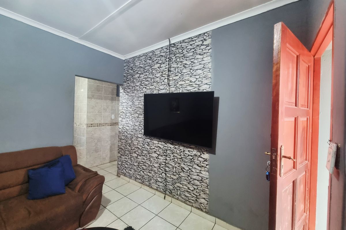 A living room featuring tiled flooring, a stone-effect feature wall, and a coved ceiling, providing a functional space with potential for aesthetic updates.