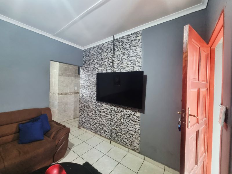 A living room featuring tiled flooring, a stone-effect feature wall, and a coved ceiling, providing a functional space with potential for aesthetic updates.