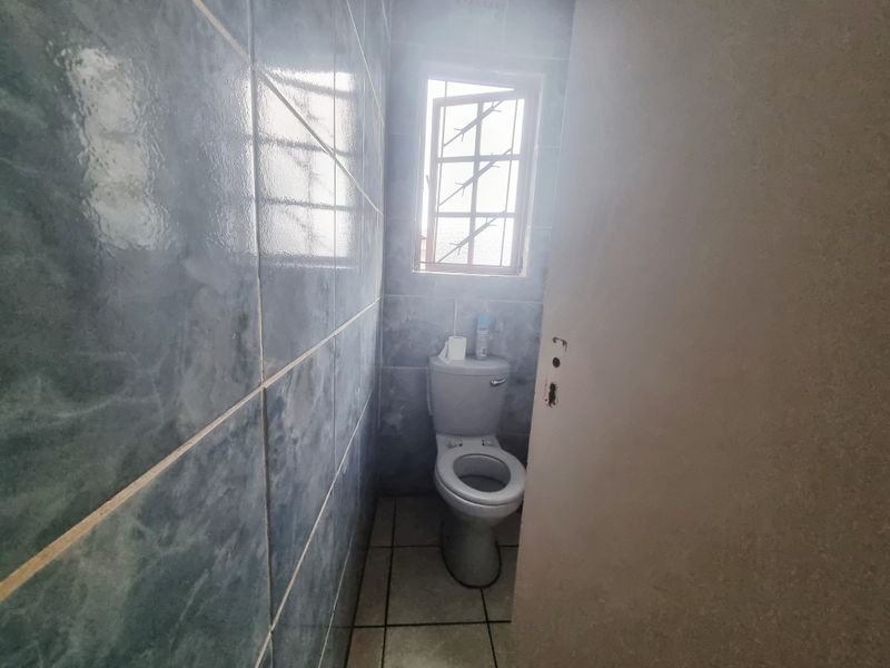 A small, tiled bathroom featuring a standard toilet and a window with security bars. The space requires minor repairs to the door hardware.