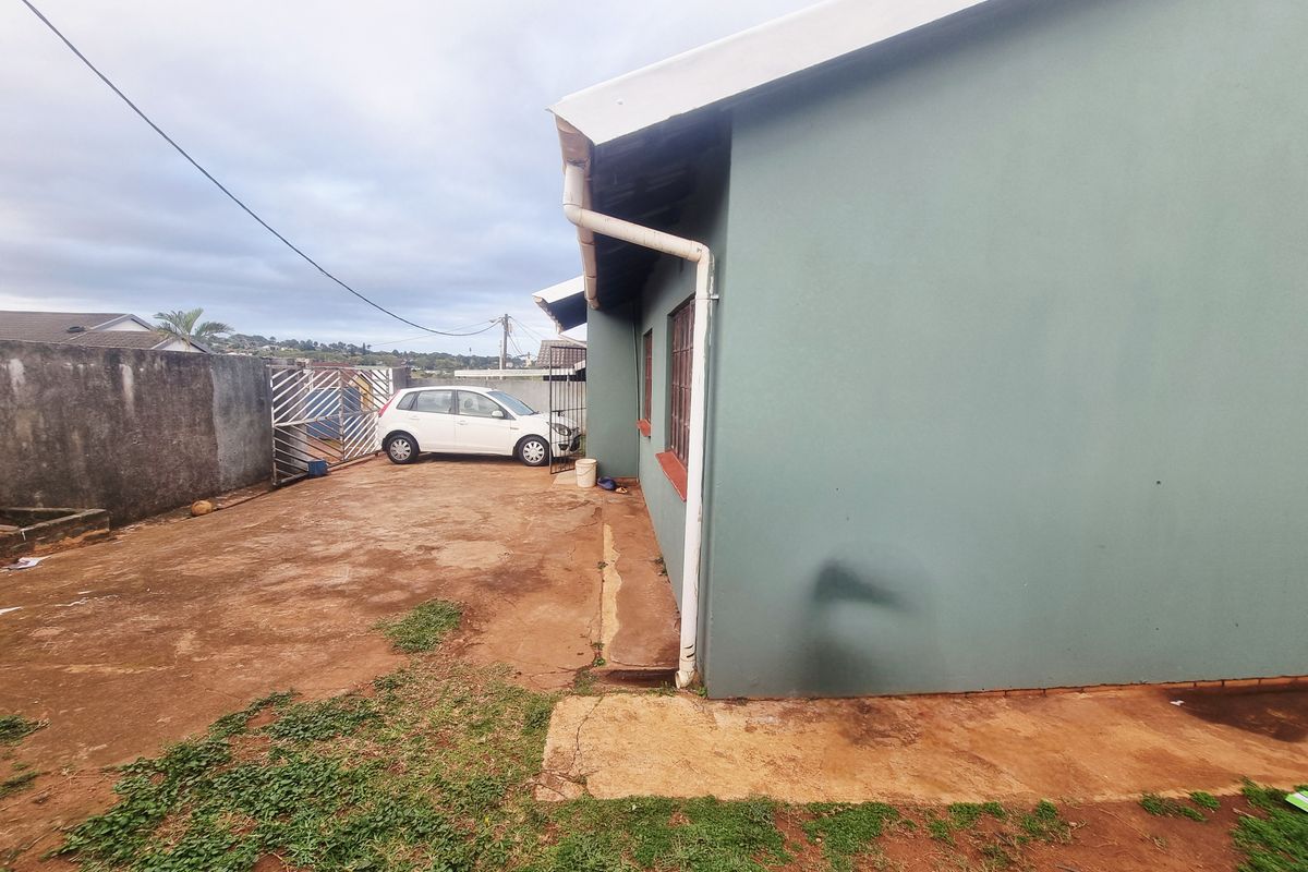 Side view of the property showing a concrete driveway, boundary wall, and exterior wall with guttering.