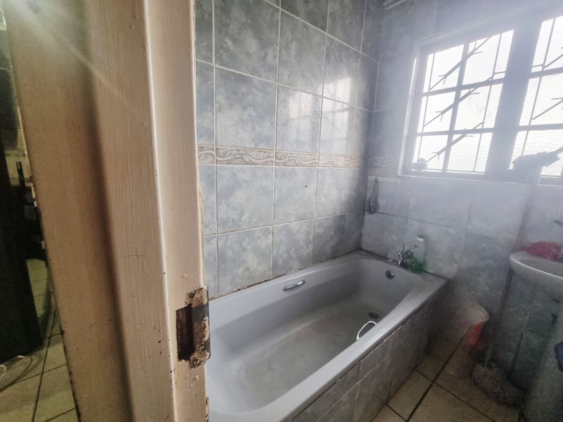 A dated bathroom featuring a standard bathtub, tiled walls, and a window with security bars, requiring cosmetic updates to improve its overall condition.