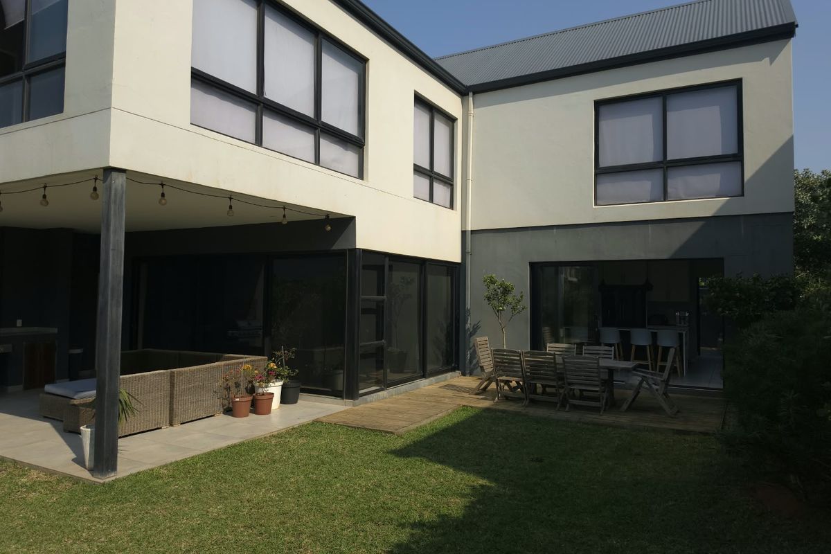 Rear view of a modern townhouse featuring a covered patio, timber decking, and a landscaped garden with large sliding glass doors.