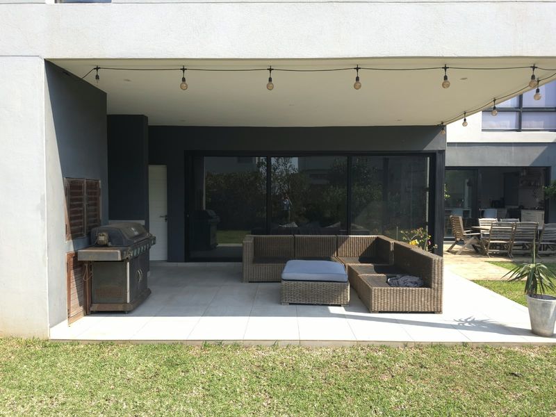 A spacious covered patio featuring large format floor tiles, recessed lighting, and seamless access to the interior through expansive sliding glass doors.