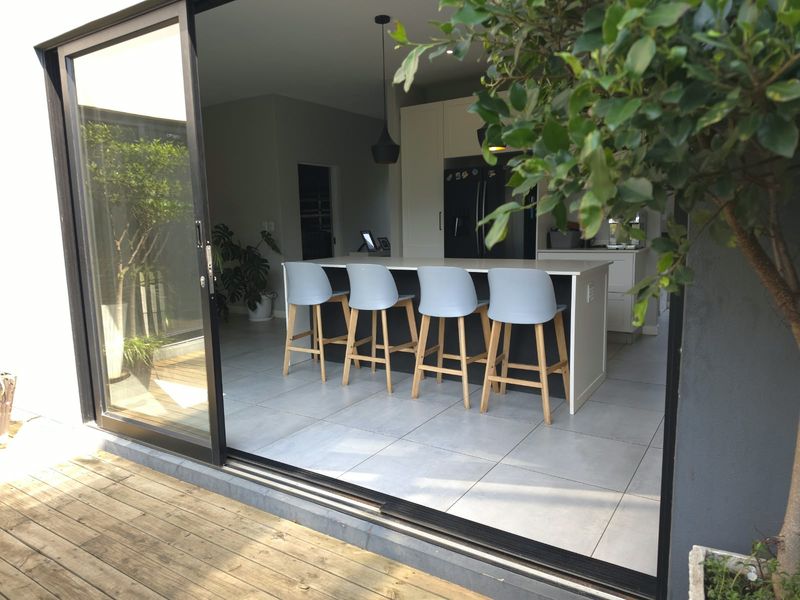 Modern open-plan kitchen featuring a central island with breakfast bar seating, seamlessly connected to the outdoor deck through large sliding glass doors.