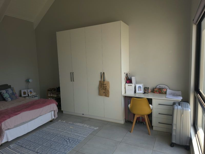 Spacious bedroom featuring a vaulted ceiling, neutral tiled flooring, and integrated built-in cabinetry with a matching desk area.