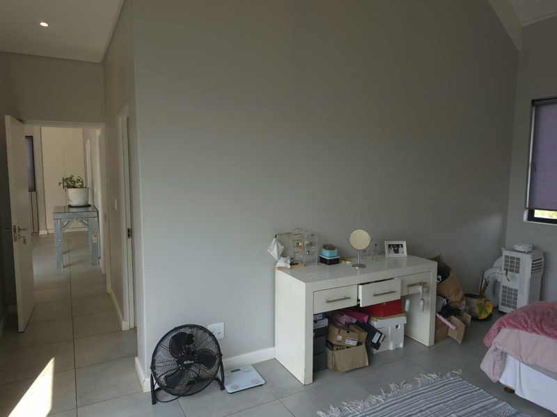 A spacious bedroom featuring neutral grey walls, tiled flooring, and recessed lighting, with a view into the adjacent hallway.