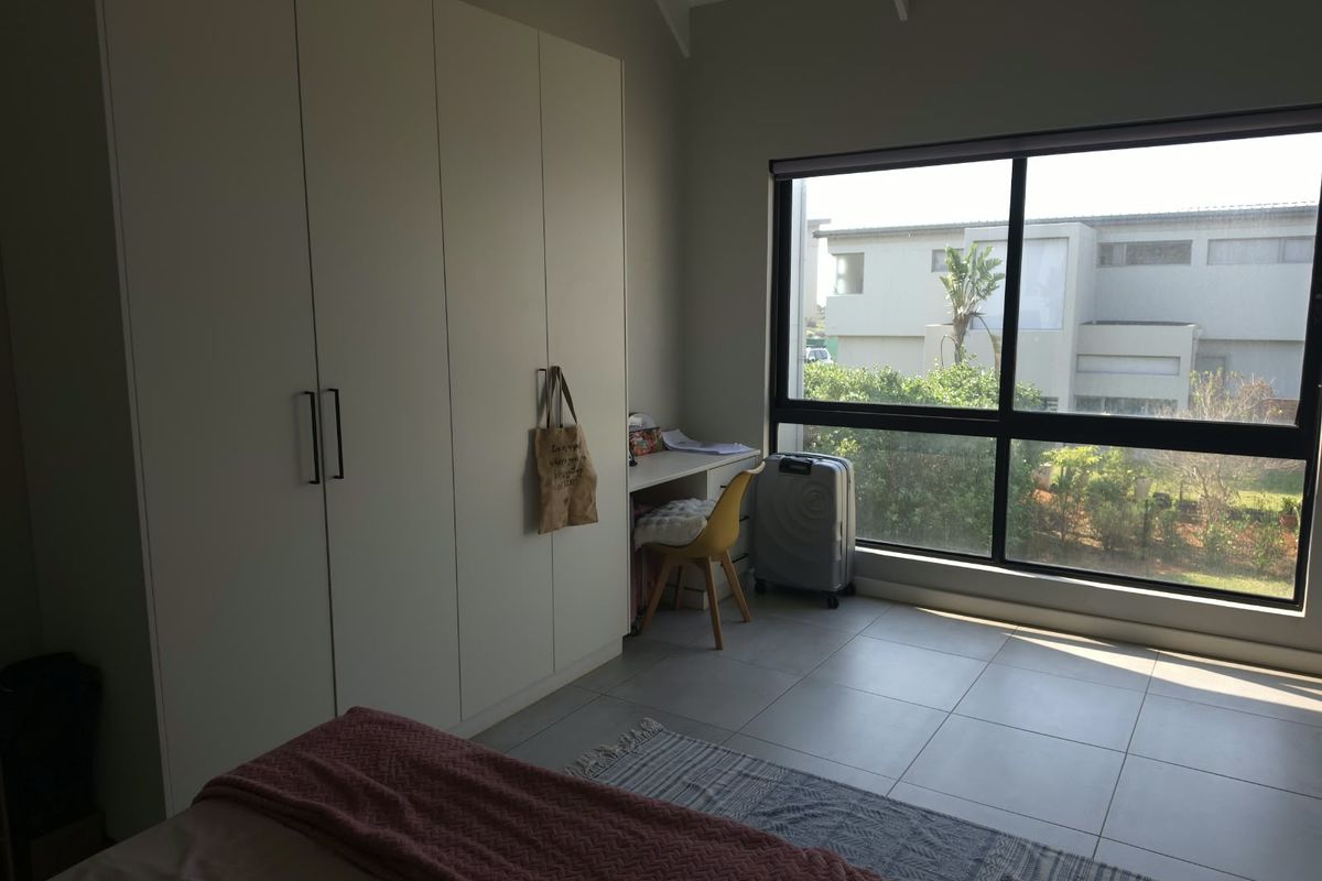 A bright bedroom featuring built-in cupboards, tiled flooring, and a large window with natural light, set under a vaulted ceiling.