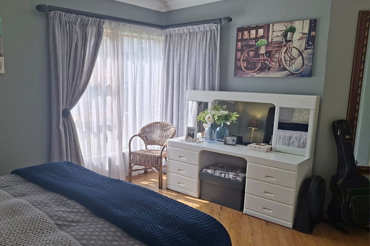 A well-maintained bedroom featuring laminate flooring, neutral wall tones, and large windows with fitted curtain rails.