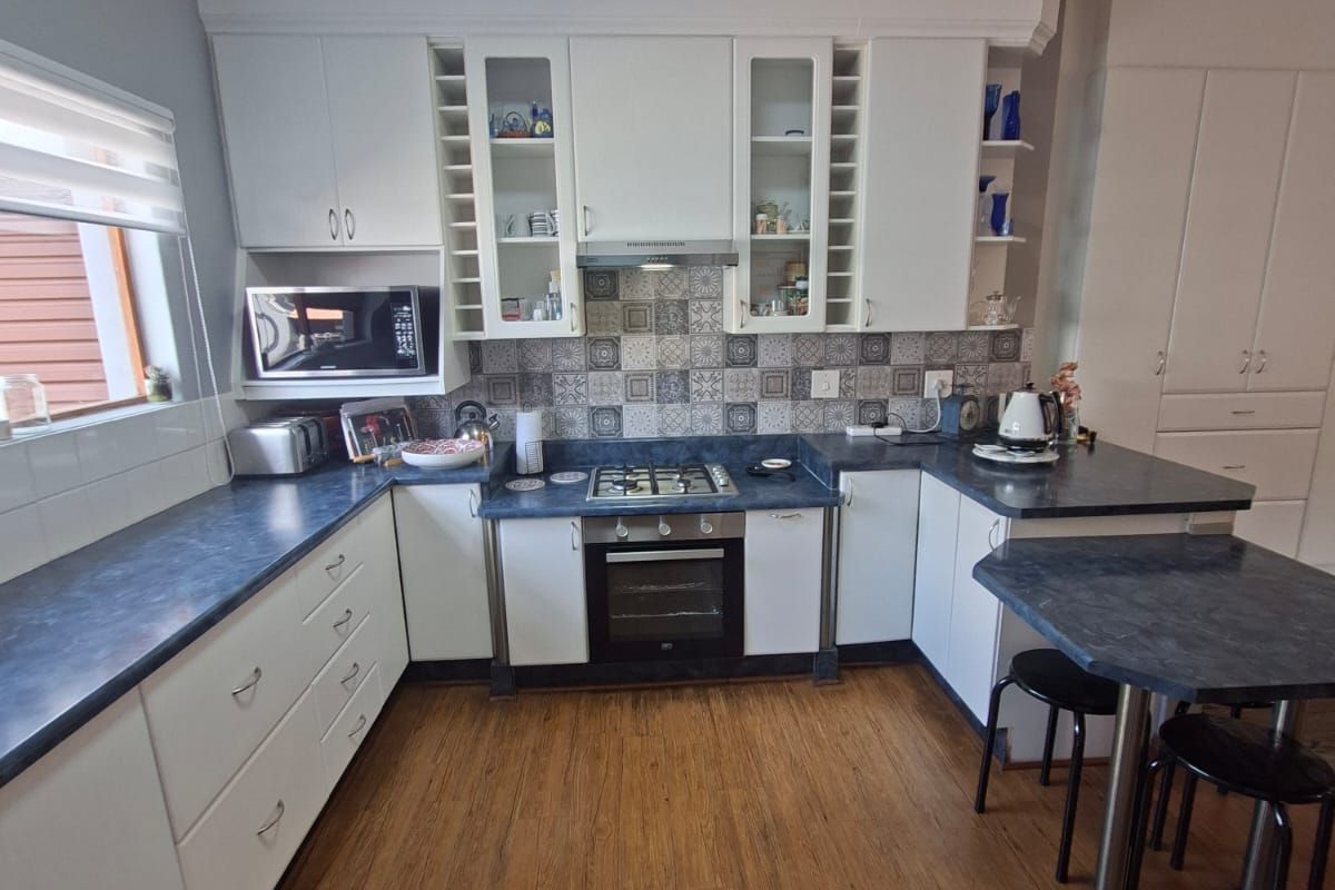 A well-maintained kitchen featuring white cabinetry, dark laminate countertops, a gas hob with extractor, and patterned tile backsplash, complemented by warm laminate flooring.