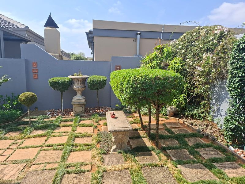 A well-maintained rear garden area featuring paved pathways, established landscaping, and a solid boundary wall.