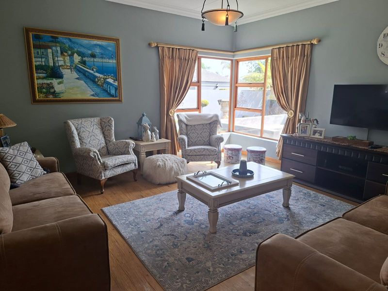 A comfortable living room featuring warm wooden flooring, large corner windows that provide natural light, and classic cornice detailing.