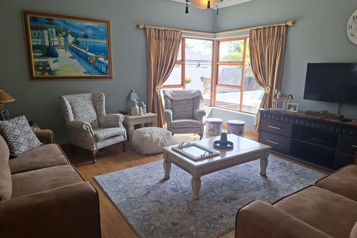 A comfortable living room featuring warm wooden flooring, large corner windows that provide natural light, and classic cornice detailing.